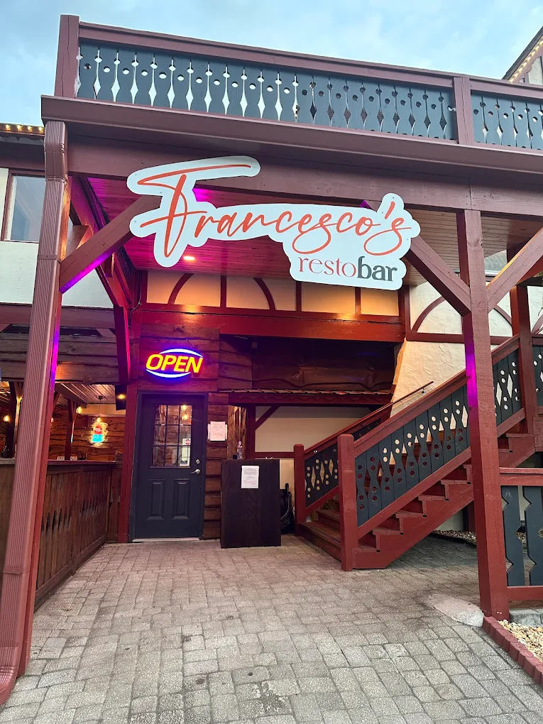 Exterior view of Francesco's Resto Bar with a wooden balcony, neon OPEN sign, and stairs leading to upper level.