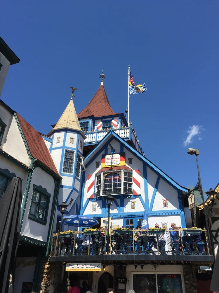 Colorful timber-framed restaurant building with blue and white walls, red roof, and an outdoor balcony filled with diners.